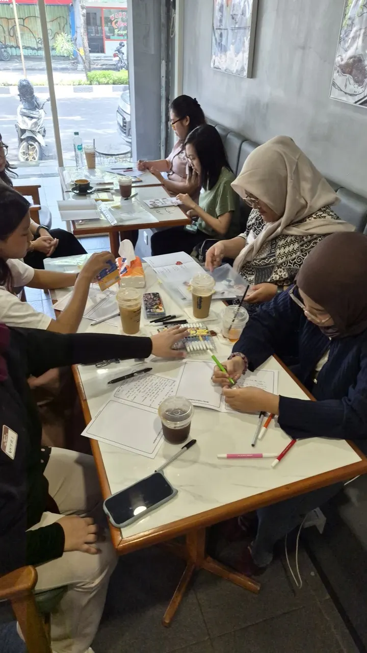 Peserta duduk melingkar di meja kafe sambil menulis dan mengerjakan lembar refleksi.